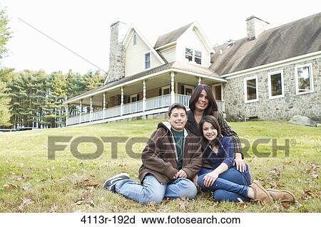 Stock Image - Portrait of smiling mother with two children sitting in front of large house. Fotosearch