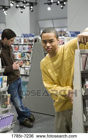 Portrait of smiling teenage boys standing amidst shelves of DVDs View Large Photo Image Stock Photograph - Portrait of smiling teenage boys standing amidst shelves of DVDs. Fotosearch