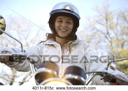 Stock Image - Portrait of smiling teenage girl sitting on motorcycle. Fotosearch