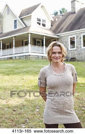 Stock Photography - Portrait of smiling woman standing in front of large house. Fotosearch