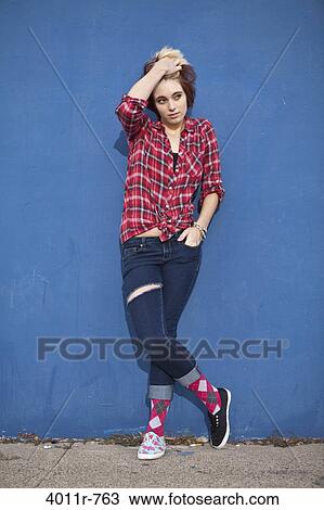 Stock Image - Portrait of teenage girl with dyed hair, wearing torn jeans, lumberjack shirt and pair of two different shoes. Fotosearch