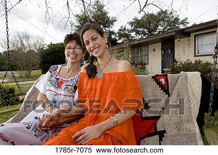 Stock Photography - Portrait of Tex-Mex mother and daughter sitting on swing in front yard of house. Fotosearch