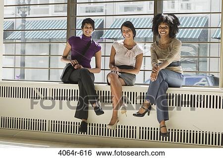 Stock Photograph - Portrait of three businesswomen sitting in office. Fotosearch