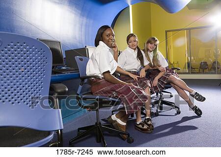 Stock Photography - Portrait of three teenage girl students wearing uniforms in a classroom. Fotosearch