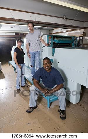 Portrait of two blue-collar men and a woman standing and sitting next two printing machines View Large Photo Image Picture - Portrait of two blue-collar men and a woman standing and sitting next two printing machines. Fotosearch