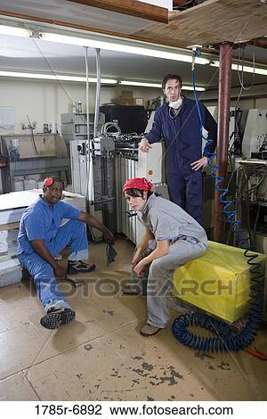 Portrait of two men and a woman in coveralls next to some machinery View Large Photo Image Stock Image - Portrait of two men and a woman in coveralls next to some machinery. Fotosearch