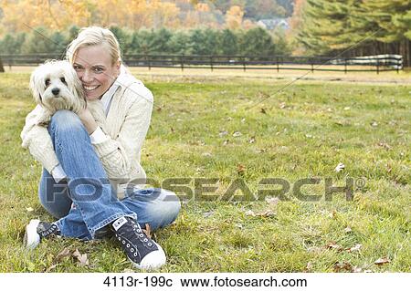 Stock Image - Portrait of woman with white dog sitting on field. Fotosearch