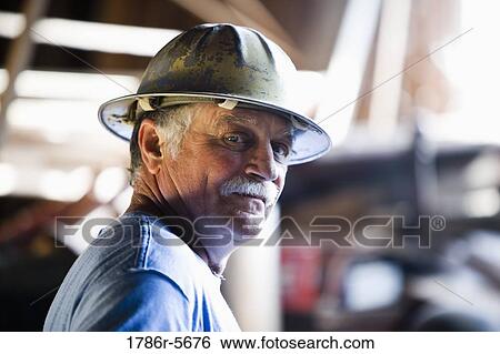 Stock Photograph - Senior man in warehouse wearing hard hat. Fotosearch