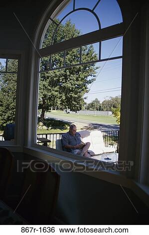 Stock Photograph - Senior man sitting outdoors reading a book. Fotosearch