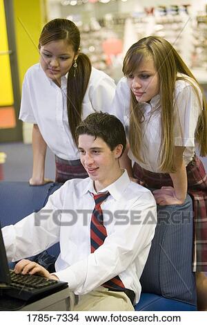 Picture - Teenage boy in school uniform using computer while girls watch. Fotosearch