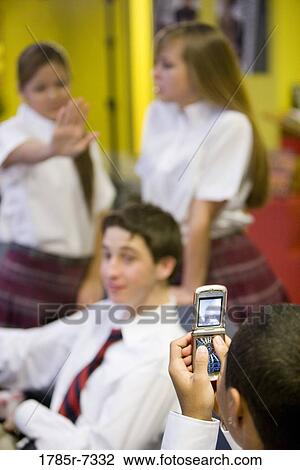 Stock Image - Teenage boy taking photograph of friends with his cell phone camera. Fotosearch