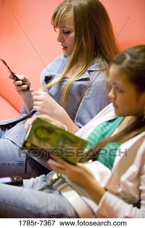 Teenage girl reading next to friend on cellphone View Large Photo Image Stock Photo - Teenage girl reading next to friend on cellphone. Fotosearch