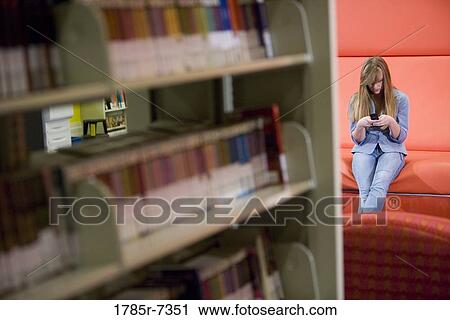 Stock Image - Teenage girl using mobile phone in library. Fotosearch