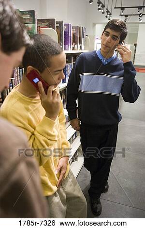 Stock Photograph - Three teenage boys talking on cell phones in a library. Fotosearch