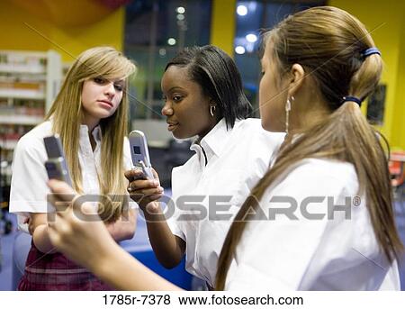 Three teenage students using mobile phone in the library View Large Photo Image Stock Photo - Three teenage students using mobile phone in the library. Fotosearch