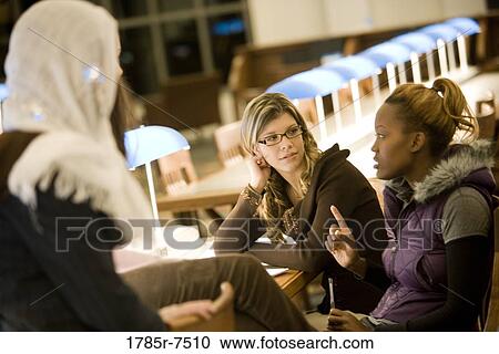 Three young women sitting and conversing in the reading room of a library View Large Photo Image Stock Image - Three young women sitting and conversing in the reading room of a library. Fotosearch
