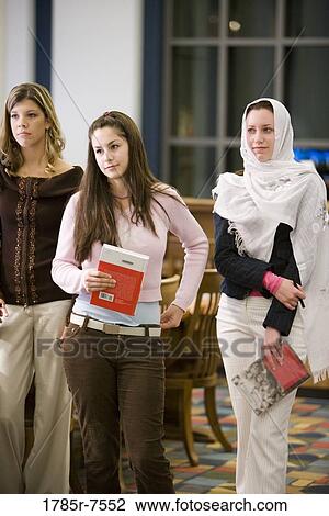 Three young women standing in the library holding books View Large Photo Image Stock Image - Three young women standing in the library holding books. Fotosearch