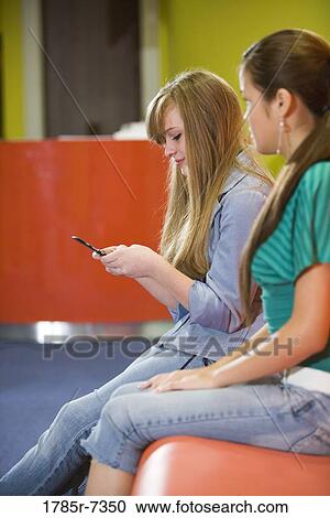 Two teenage girlfriends sitting together, using a cell phone View Large Photo Image Stock Image - Two teenage girlfriends sitting together, using a cell phone. Fotosearch