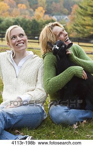 Stock Image - Two women with black lamb sitting on field. Fotosearch