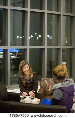 Two young women conversing while sitting on sofa View Large Photo Image Stock Image - Two young women conversing while sitting on sofa. Fotosearch