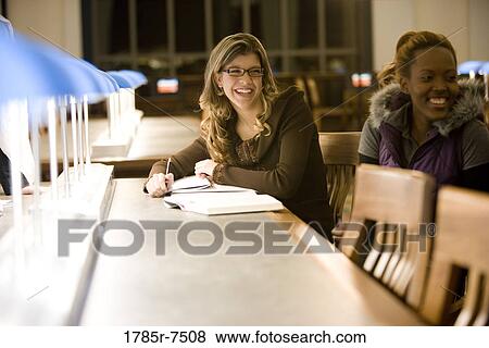 Two young women sitting and conversing in the reading room of a library View Large Photo Image Stock Photo - Two young women sitting and conversing in the reading room of a library. Fotosearch