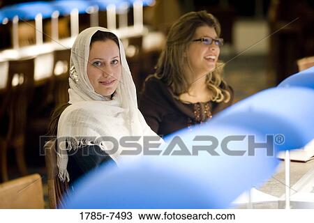 Two young women sitting in the reading room of a library View Large Photo Image Stock Image - Two young women sitting in the reading room of a library. Fotosearch