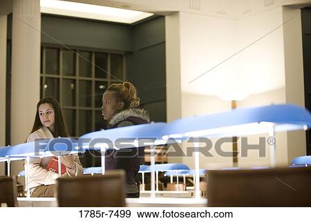 Two young women sitting in the reading room of a library View Large Photo Image Stock Photo - Two young women sitting in the reading room of a library. Fotosearch
