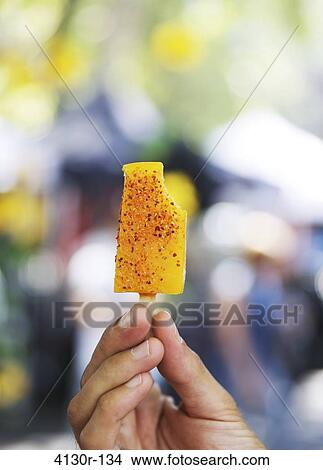 Picture - USA, New York State, New York City, Hester Street Market, La NewYorkina, Hand holding mango ice lolly with chili powder. Fotosearch