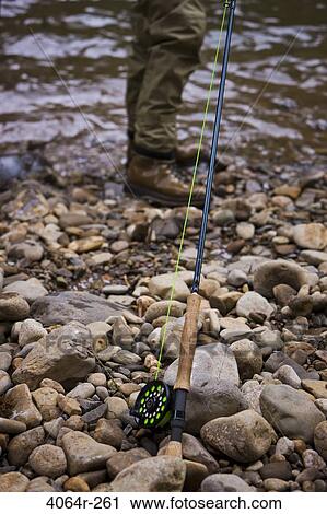 Stock Image - USA, Washington, Vancouver, Fishing rod on pebbled riverbank, man standing in background. Fotosearch