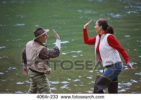 Stock Image - USA, Washington, Vancouver, Fishing couple giving high five by river. Fotosearch