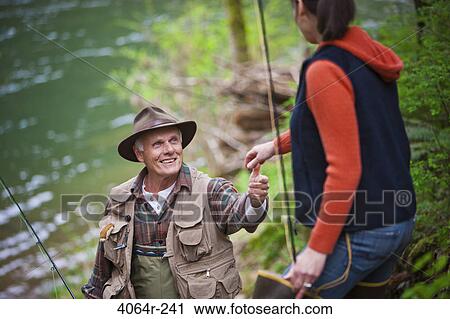 Stock Image - USA, Washington, Vancouver, Smiling couple with fishing rods by river. Fotosearch