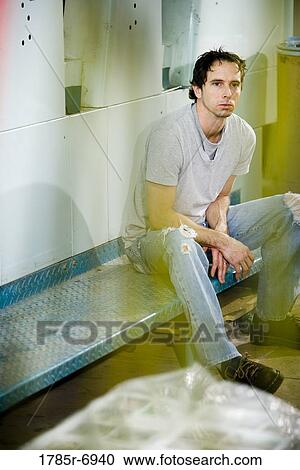 Stock Image - View of a blue-collar man sitting in front of some machinery. Fotosearch