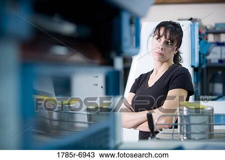 Stock Image - View of a blue-collar woman standing behind some machinery. Fotosearch
