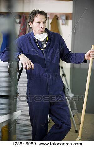 View of a man in coveralls holding a broom in a warehouse View Large Photo Image Stock Photo - View of a man in coveralls holding a broom in a warehouse. Fotosearch