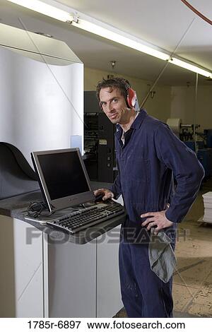 View of a man in coveralls operating a machine by using a computer View Large Photo Image Stock Photo - View of a man in coveralls operating a machine by using a computer. Fotosearch
