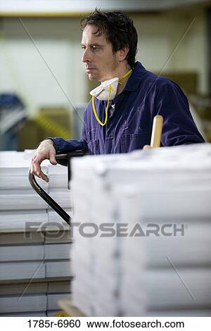 View of a man in coveralls standing amidst stacks of material in a warehouse View Large Photo Image Stock Image - View of a man in coveralls standing amidst stacks of material in a warehouse. Fotosearch