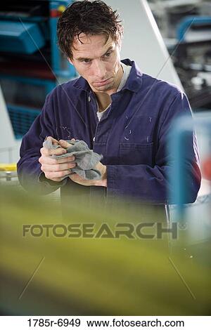 View of a man in coveralls wiping his hands in front of some machinery View Large Photo Image Stock Photo - View of a man in coveralls wiping his hands in front of some machinery. Fotosearch