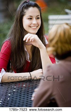 Stock Image - View of a smiling young woman sitting at a table. Fotosearch