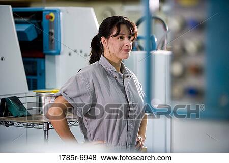View of a woman in coveralls standing in front of some machinery View Large Photo Image Stock Photo - View of a woman in coveralls standing in front of some machinery. Fotosearch