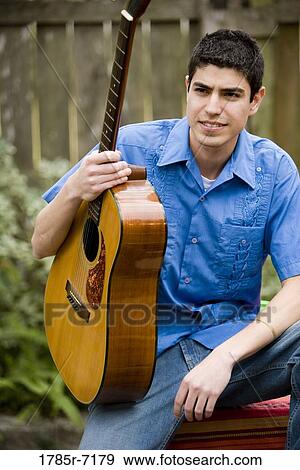 View of a young man holding a guitar View Large Photo Image Stock Photo - View of a young man holding a guitar. Fotosearch