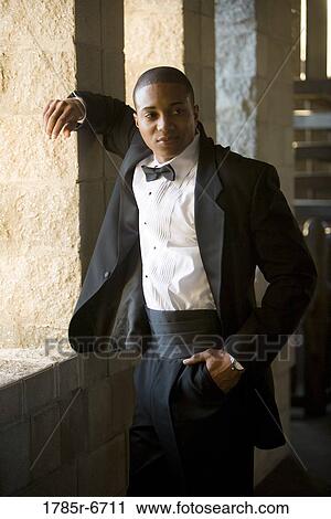 Stock Image - View of a young man in a black tuxedo leaning against a large window inside a medieval castle. Fotosearch