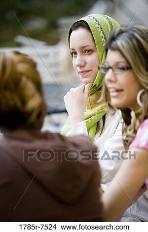 View of a young woman wearing a head scarf sitting with her friends View Large Photo Image Picture - View of a young woman wearing a head scarf sitting with her friends. Fotosearch
