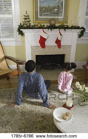 Stock Photograph - View of brother and sister sitting by fireplace decorated for Christmas, waiting for Santa. Fotosearch