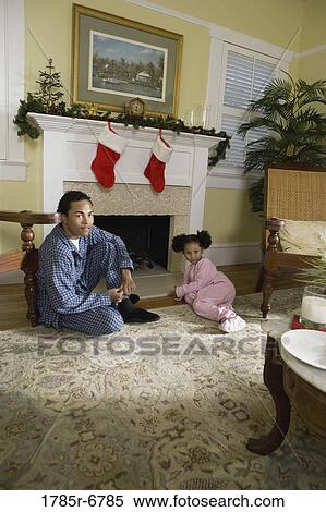 Stock Photography - View of brother and sister sitting by fireplace decorated for Christmas, waiting for Santa. Fotosearch