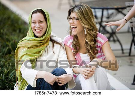 View of two cheerful young women sitting on a curb outside a building View Large Photo Image Stock Photo - View of two cheerful young women sitting on a curb outside a building. Fotosearch
