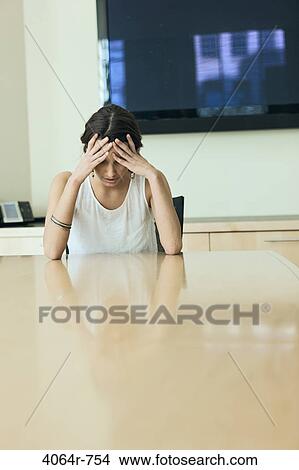 Picture - Woman sitting with head in hands at boardroom table. Fotosearch