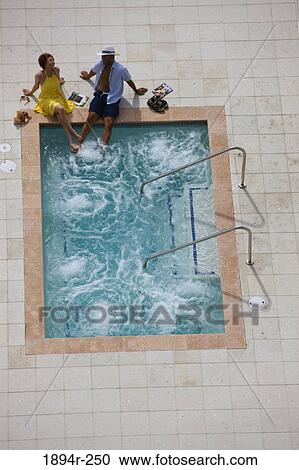 Stock Image - Young couple sitting at the poolside. Fotosearch