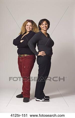 Stock Image - Young female friends smiling while posing. Fotosearch