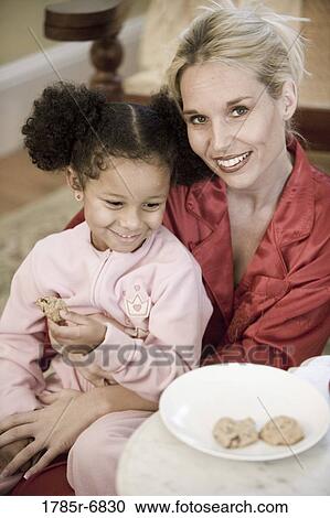 Young girl dressed in pajamas sitting on her mother's lap eating a cookie View Large Photo Image Stock Image - Young girl dressed in pajamas sitting on her mother's lap eating a cookie. Fotosearch