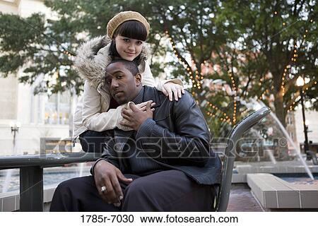 Young inter-racial couple embracing on a park bench View Large Photo Image Stock Image - Young inter-racial couple embracing on a park bench. Fotosearch